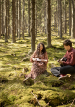 Na zdjęciu dwie osoby siedzące na polanie w lesie.