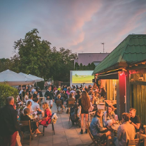 Ludzie siedzą wieczorem przy stolikach, rozmawiają.