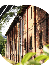 Budynek z czerwonej cegły, otoczony zielenią.