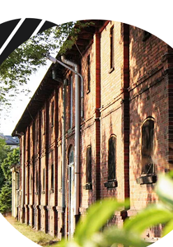 Budynek z czerwonej cegły, otoczony zielenią.