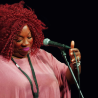 Na zdjęciu ciemnoskóra wokalistka w różowej bluzce.