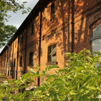Budynek z czerwonej cegły, otoczony zielenią.