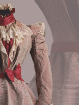 Czerwona suknia z XIX wieku z czerwoną kokardą w pasie i koronkami.