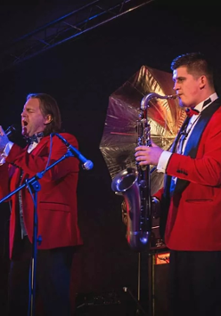 Dwójka mężczyzn. ubranych na czerwono, jedna śpiewa drugi gra na saksofonie.