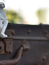 Zdjęcie przedstawiające małą figurkę człowieka siedzącą na walizce, po prawej informację dotyczące wystawi fotografii "Zatrzymani w podróży".