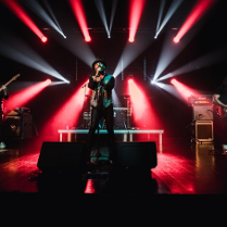 Na zdjęciu artysta śpiewający na scenie na tle czerwono białych świateł.