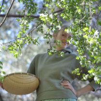 Zdjęcie na pierwszym planie ma gałązki drzewa, na dalszym uśmiechniętą młodą kobietę.