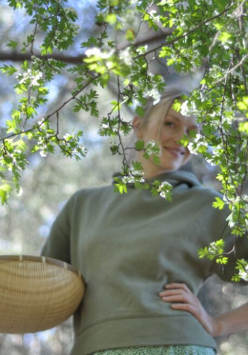 Zdjęcie na pierwszym planie ma gałązki drzewa, na dalszym uśmiechniętą młodą kobietę.