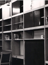 Czarno-białe zdjęcie drewnianej meblościanki. Na półkach widoczne są książki i stare radio.