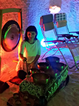 Zdjęcie przedstawia kobietę grającą na misach; za jej plecami widoczny jest gong oraz leżaki.