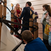 Grupa ludzi stoi na schodach Biblioteki i słucha przewodniczki.