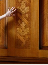 Dłoń na tle drewnianego panelu z intarsją w kształcie dębowych liści.