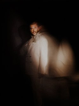 Rozmazana sylwetka artysty na ciemnym tle.