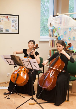 Na zdjęciu dwie siedzące kobiety, grające na wiolonczelach.