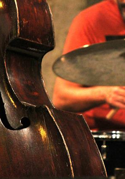 Zdjęcie na którym widać część kontrabasu. w tle muzyk przy perkusji.