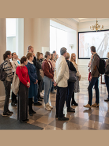Uczestnicy stoją w holu Biblioteki i słuchają przewodnika.