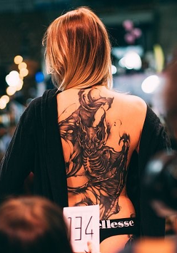 Kobieta z wytatułowanymi plecami stoi tyłem do jury.