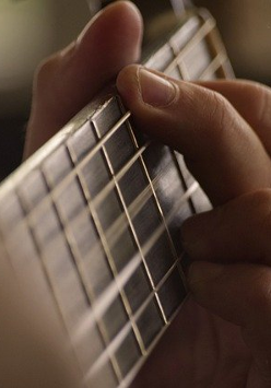 Zdjęcie gryfu i dłoni z chwytem gitarowym.