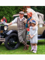 Zdjęcie rodziny (mężczyzna, kobieta i córka) ubranych w stylu epoki międzywojnia, w tle zabytkowe auto.