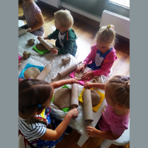 Zdjęcie przedstawia grupkę małych dzieci wałkujących kawałki gliny.