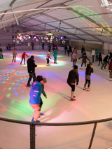 kilkanaście osób jeżdżących na łyżwach na krytym lodowisku