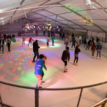 kilkanaście osób jeżdżących na łyżwach na krytym lodowisku