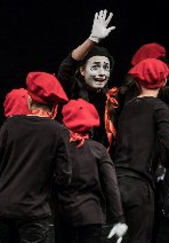 grupa dzieci w czarnych koszulkach i czerwonych beretach wraz z aktorem z umalowana na biało twarzą