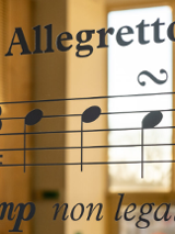 Zdjęcie pięciolini z nutami. Nad nimi napis allegretto. w tle rozmyte okno.