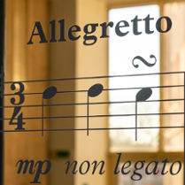 Zdjęcie pięciolini z nutami. Nad nimi napis allegretto. w tle rozmyte okno.