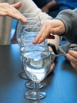 zdjecie kilku kieliszkow napelnionych wodą i dlonie dziecka trzymajacego metalowa lyzeczke