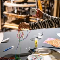 ręce dziecka trzymającego szpule z wstązką na stołem z innymi materiałami plastycznymi