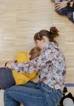 Na zdjęciu fragment warsztatów dla dzieci. Na podłodze leżą dorośli przytulając dzieci.