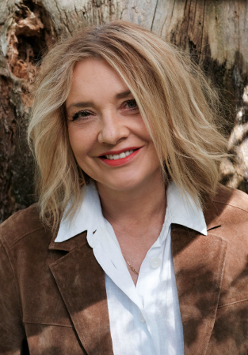 na zdjęciu uśmiechnięta kobieta z włosami do ramion, w białej bluzce i jasnej kurtce