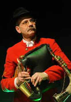 Na zdjęciu dudziarz w czerwonym ubraniu trzymający instrument muzyczny.