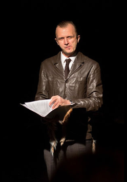 Na zdjęciu mężczyzna w brązowej skórzanej kurtce. W dłoniach trzyma teczkę, patrzy w obiektyw.