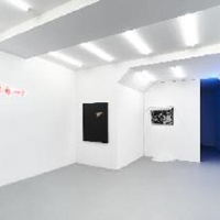 Zdjęcie z wystawy. Minimalistyczna biała przestrzeń galerii, na ścianach wiszą obrazy.