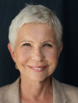 Zdjęcie uśmiechniętej kobiety w średnim wieku, ubranej w białą buzkę i beżową marynerkę w kratę.