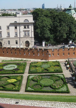 Francuskie ogrody otoczone ceglastym murem, za nim kamienice i ulica. Widok z góry.