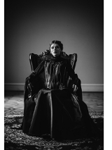 zdjęcie przedstawia kobietę w czarnej sukni siedzącą na wysokim czarnym fotelu