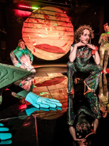 Zdjęcie trzech aktorów na scenie wśród elementów scenicznych dekoracji.