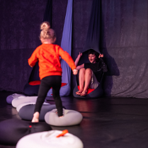 na scenie, w wiszącym kokonie siedzi kobieta, do niej biegnie zwrócone tyłem do obiektywu dziecko