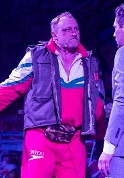 Dwóch mężczyzn stojących naprzeciwko siebie, jeden eleganco ubrany w garnitur, drugi w sportowym dresie i ortalionowej kamizelce.