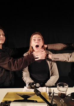 Na zdjęciu trzy osoby, dwie trzymają za szyję osobę w środku, dusząc ją.