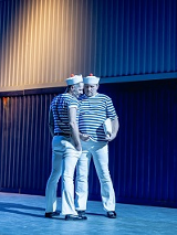 Na scenie dwóch mężczyzn stojących blisko siebie, w strojach przypominających marynarskie. Zdjęcie w niebiesko-błękitnych kolorach.