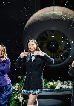 Trzy uśmiechające się kobiety stoją na tle zdjęcia wielkiej gałki ocznej.