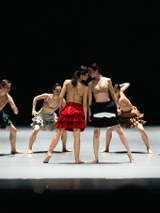 Scena ze spektaklu - tancerze na scenie, w środku dwie tancerki blisko siebie, dotykają się głowami.