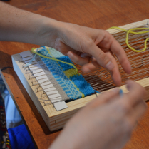 Dłonie wyplatające kolorową tkaninę na ręcznym, prostym krośnie.