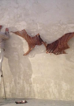 Zdjęcie artysty wieszającego swoją pracę na ścianie galerii.