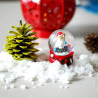 na stole: śnieg, szyszki i Mikołaj w szklanej kuli.