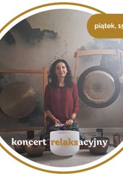 Kobieta w średnim wieku z czarnymi włosami. Ubrana w czerwony długi rękaw i wzorzyste spodnie. Siedzi na podłodze. Za nią wiszą 2 gongi. Przed nią leży kilka mis.